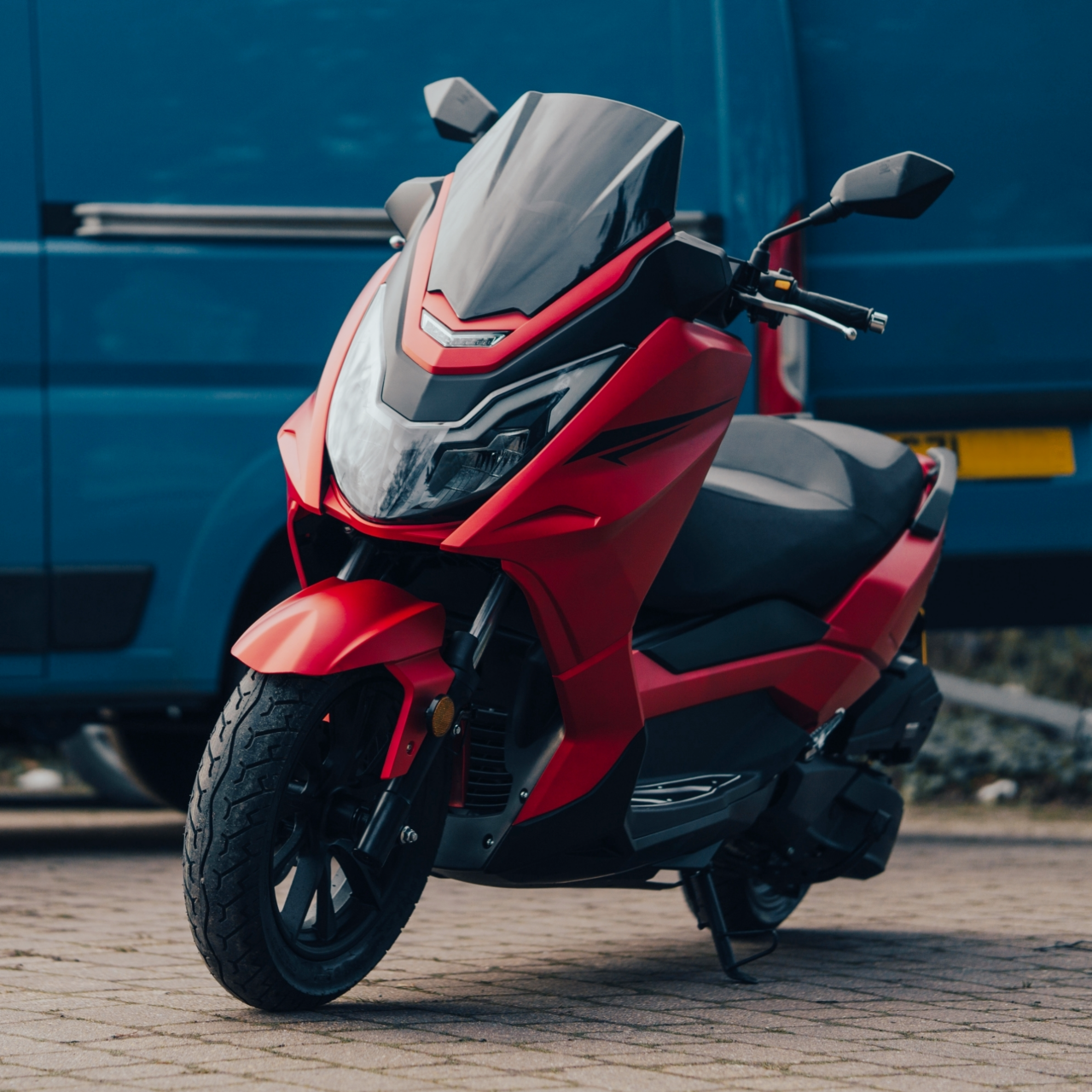 Red maxi scooter being delivered parked next to a blue delivery van,